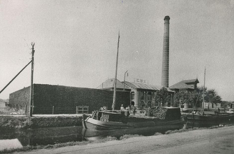 <p>De Molenstreek in Veendam met aan de overkant de Turfcentrale en in het water enkele turfschepen. Links naast de centrale een enorme bult turf. &ndash; Foto: collectie Veenkoloniaal Museum Veendam</p>
