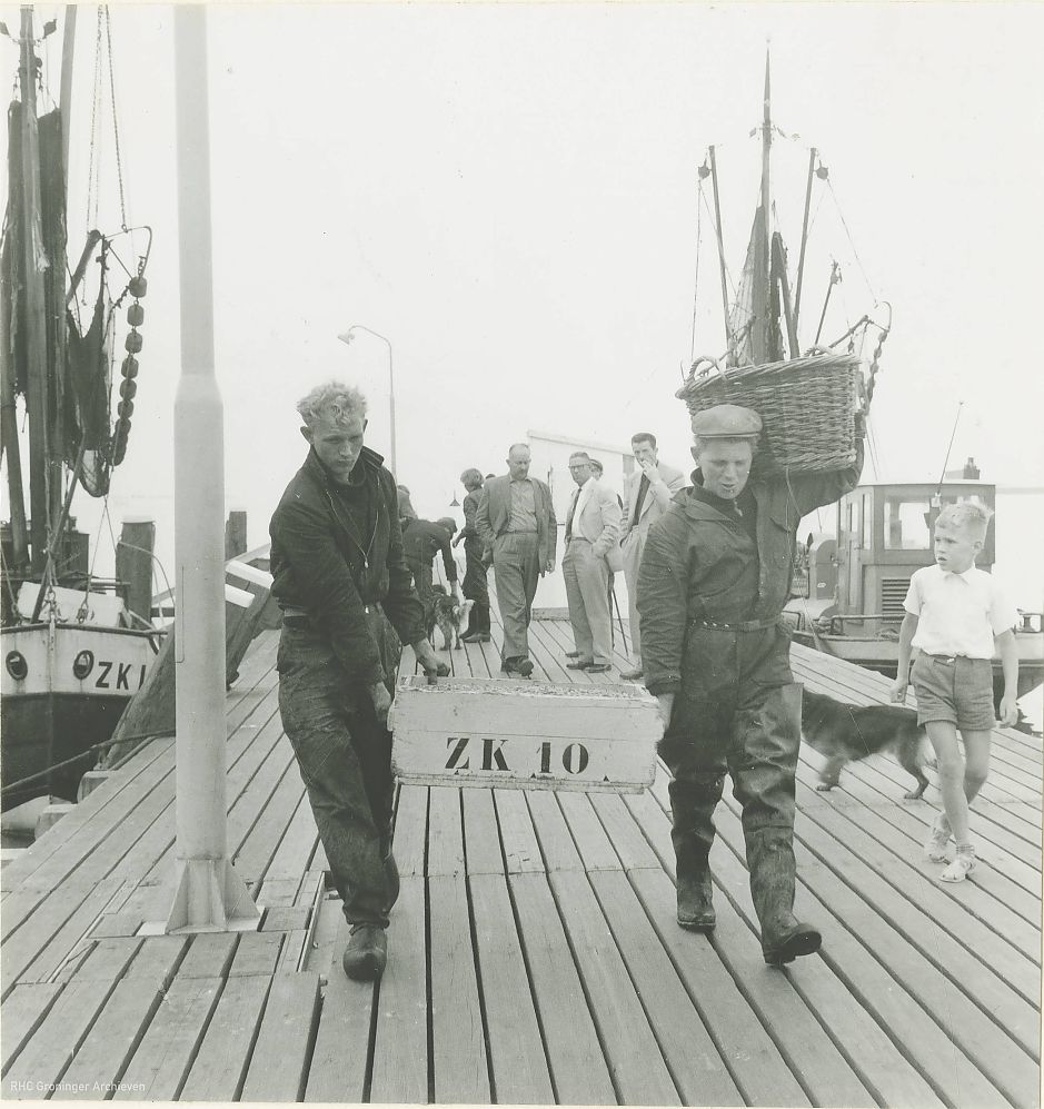 <p>Zoutkamp: Twee jongemannen brengen de vangst van de vissersboot ZK10 aan land, ca. 1960 - Foto: Collectie VVV, collectie Groninger Archieven</p>
